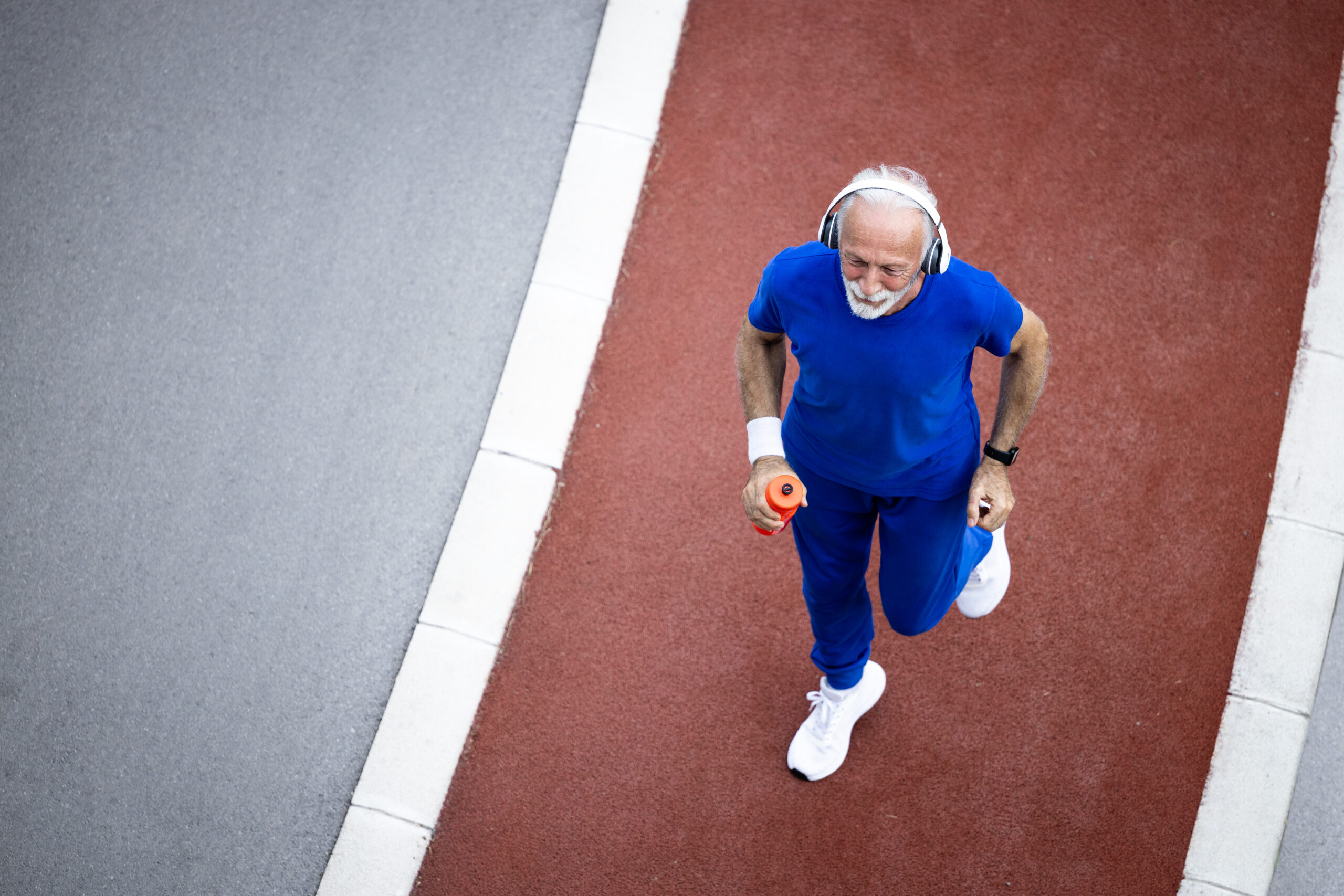 Top view of top shaped senior man running on track. Exercising in retirement for good health.